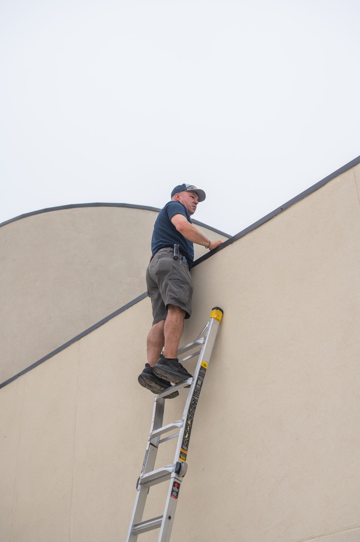 Home inspector on a ladder inspecting the roof edge and flashing of a Taylor, TX home
