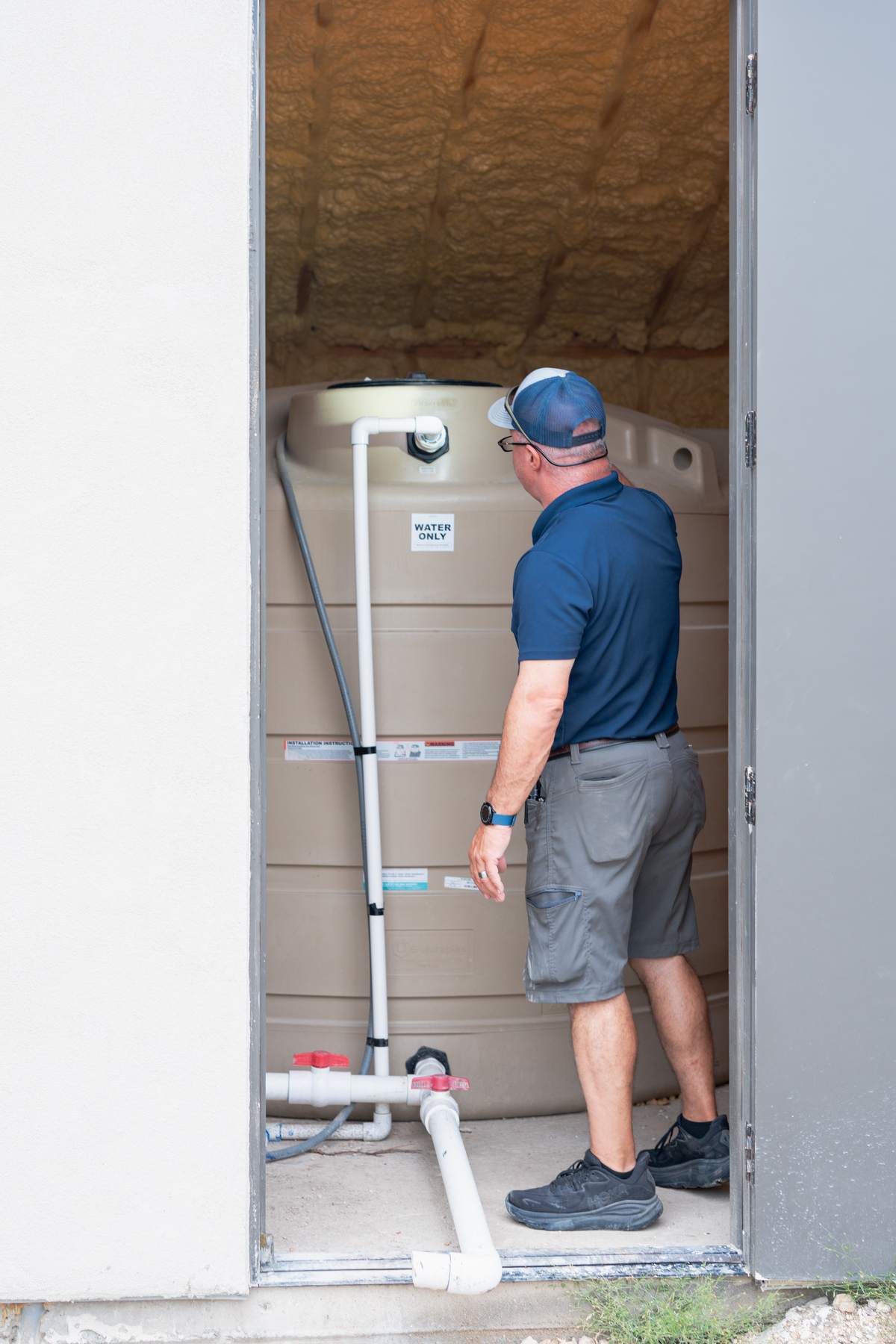Inspector inspecting a water storage tank and supply plumbing at a rural property